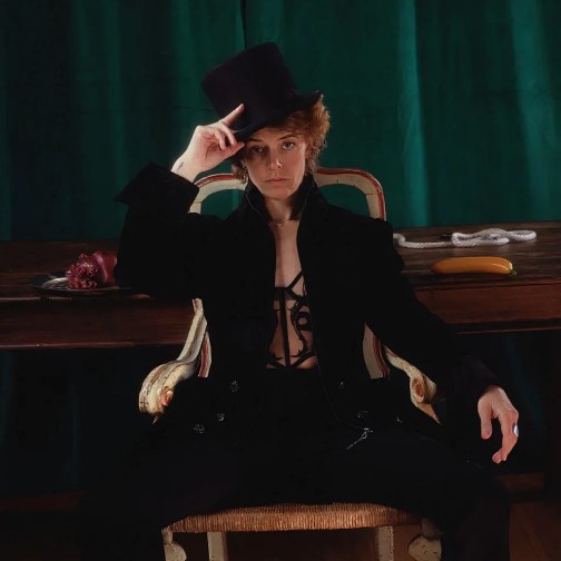 Ellie J as Clown Daddy wearing a top hat and black formal attire, sitting in a chair.